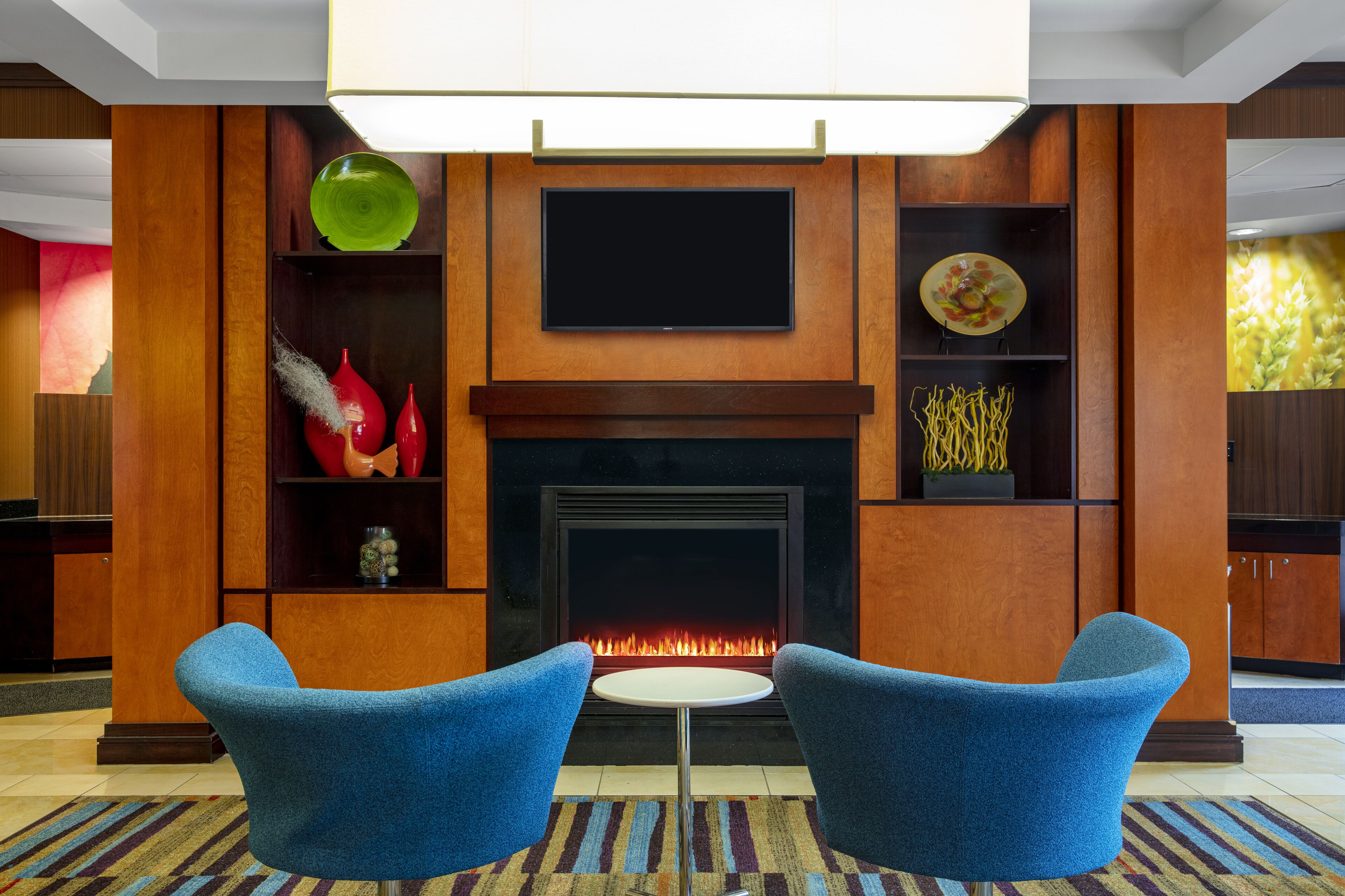 A modern living room with a fireplace, two blue armchairs, a flat-screen TV, and decorative items on shelves.