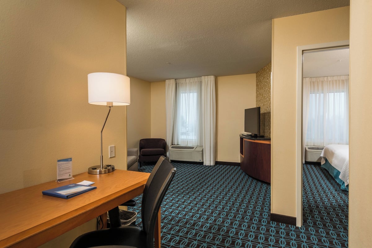 A hotel room with a desk, chair, TV, and a bed.