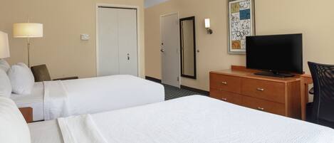Una habitación de hotel con dos camas, televisión, cómoda y lámpara.