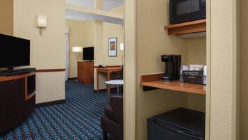 A hotel room with a television, a desk, a chair, a microwave, and a coffee maker.