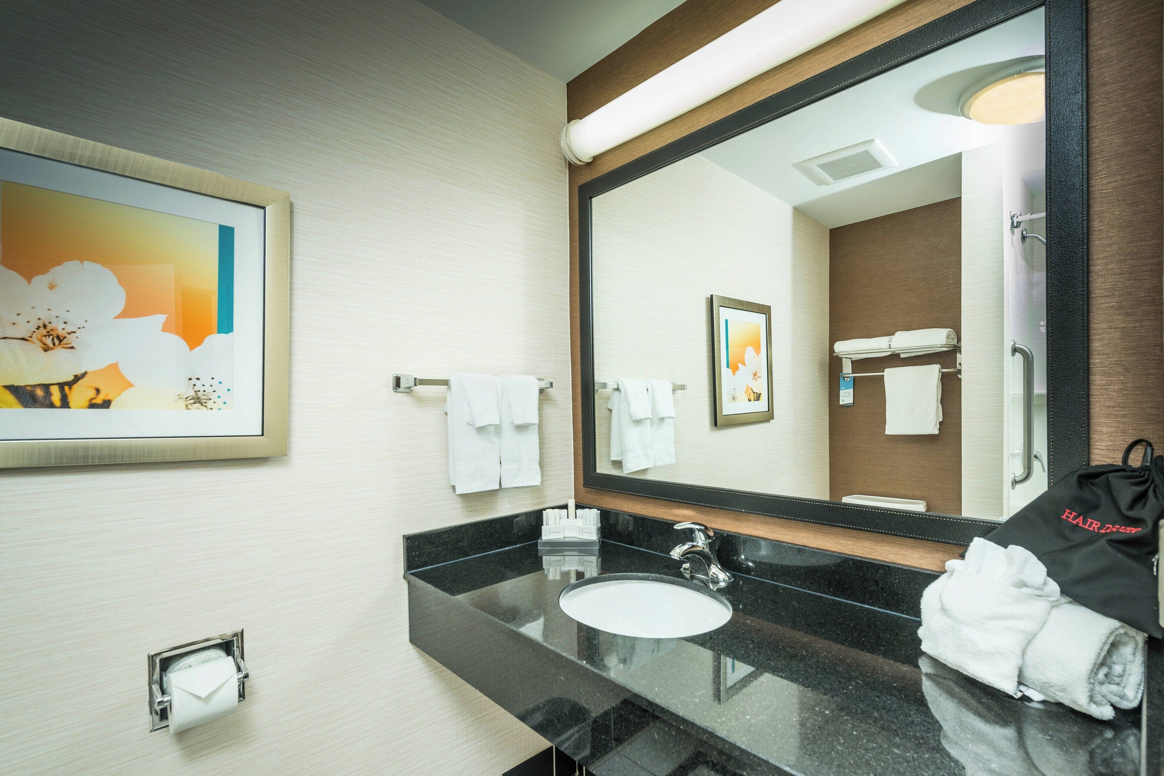 Un baño moderno con lavamanos de superficie negra, un espejo grande y una obra de arte floral enmarcada en la pared.