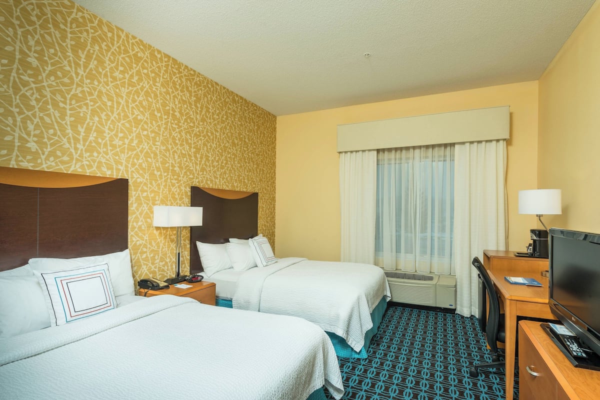 A hotel room with two beds, a desk, a television, and a window with curtains.