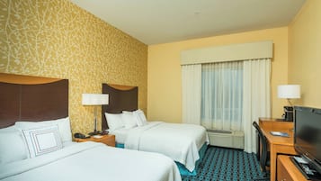 A hotel room with two beds, a desk, a television, and a window with curtains.
