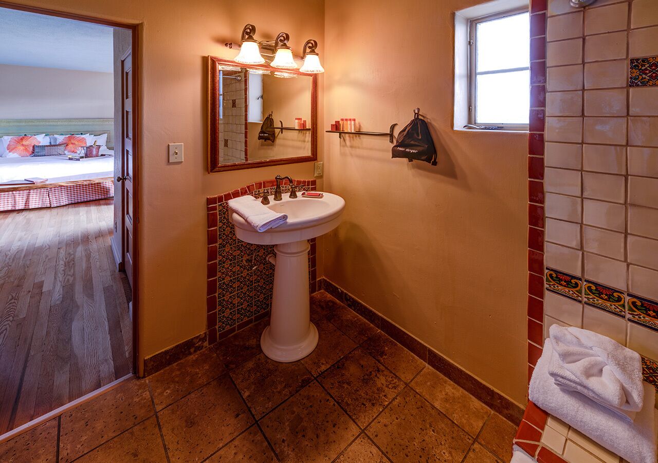 Een badkamer met een wit wastafeltje, een spiegel en een raam.
