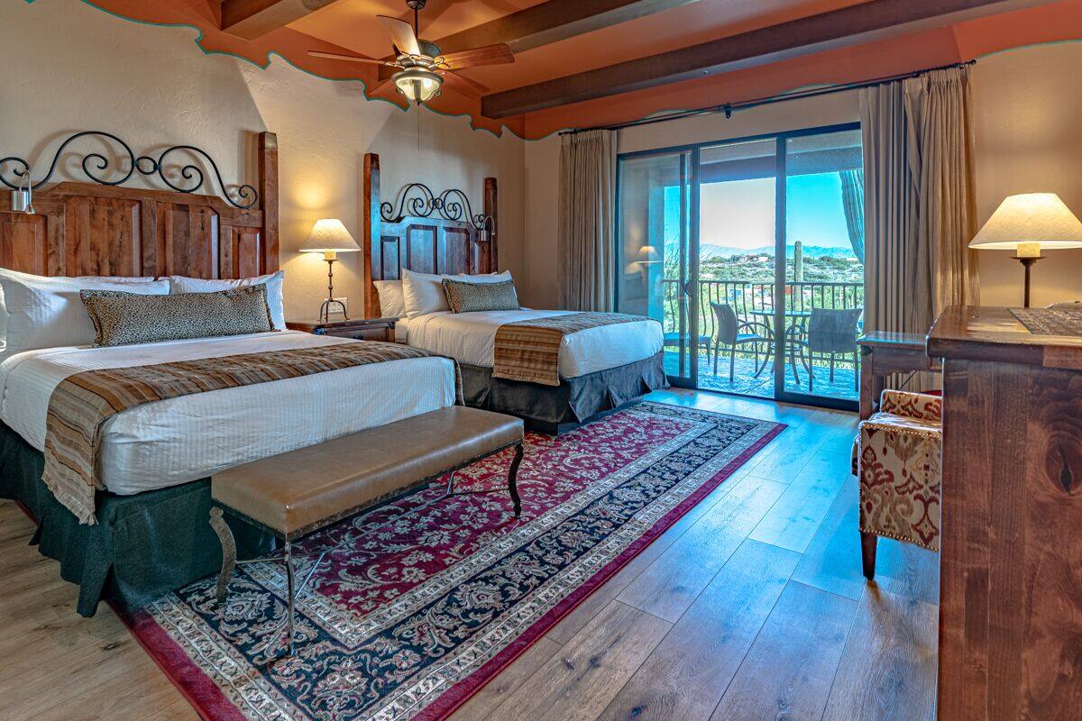 Une chambre d’hôtel avec deux lits, un balcon avec des chaises, un plafond en bois et une grande fenêtre.