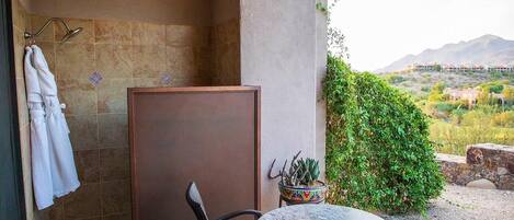 A bathroom with a shower, a towel rack, a potted plant, and a table.