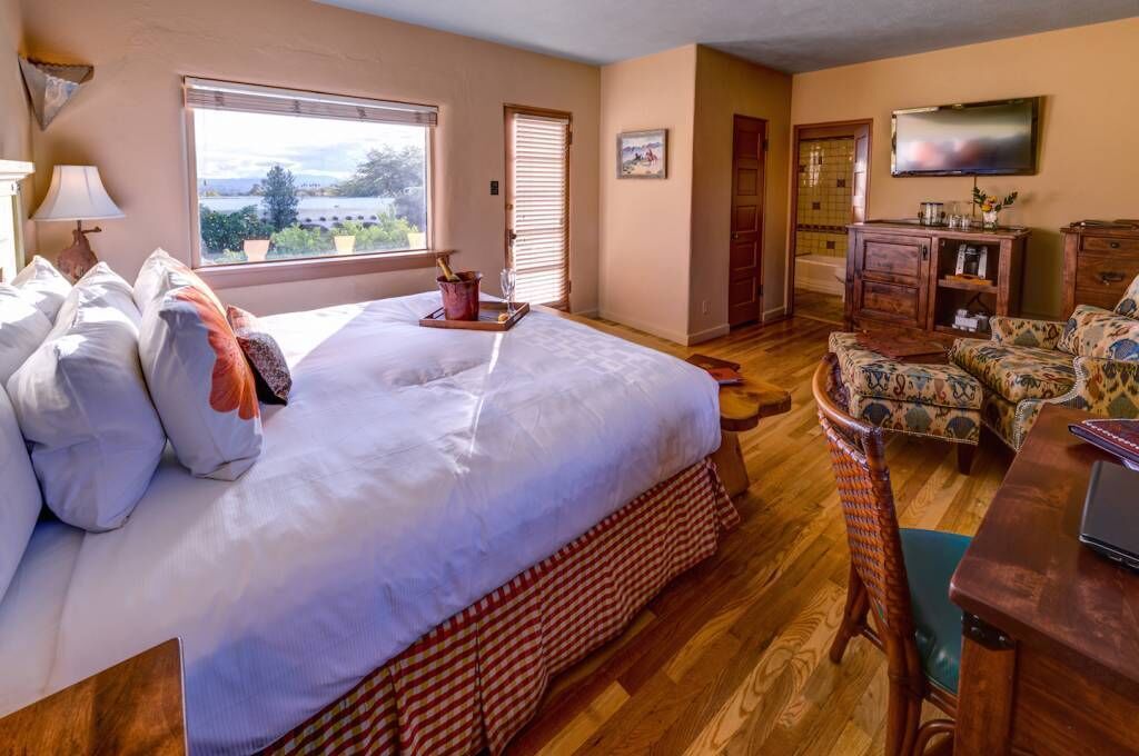 A bedroom with a large bed, a wooden dresser, a television, and a view of the outdoors.