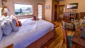 A bedroom with a large bed, a wooden dresser, a television, and a view of the outdoors.