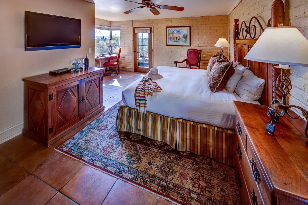 A hotel room with a bed, a wooden dresser, a television, a desk, and a chair.