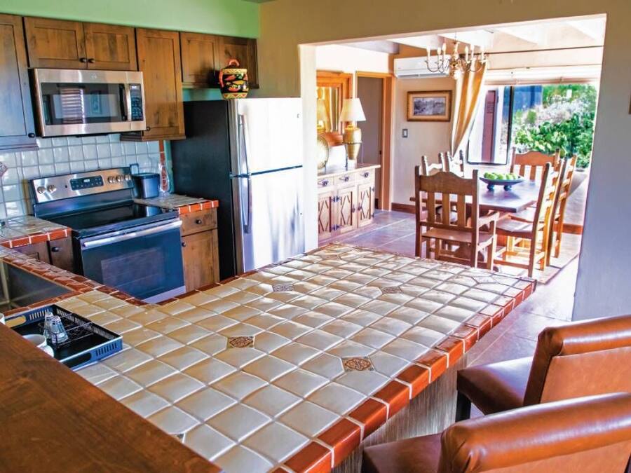 A kitchen with a central island, wooden cabinets, and a dining area with chairs and a table.