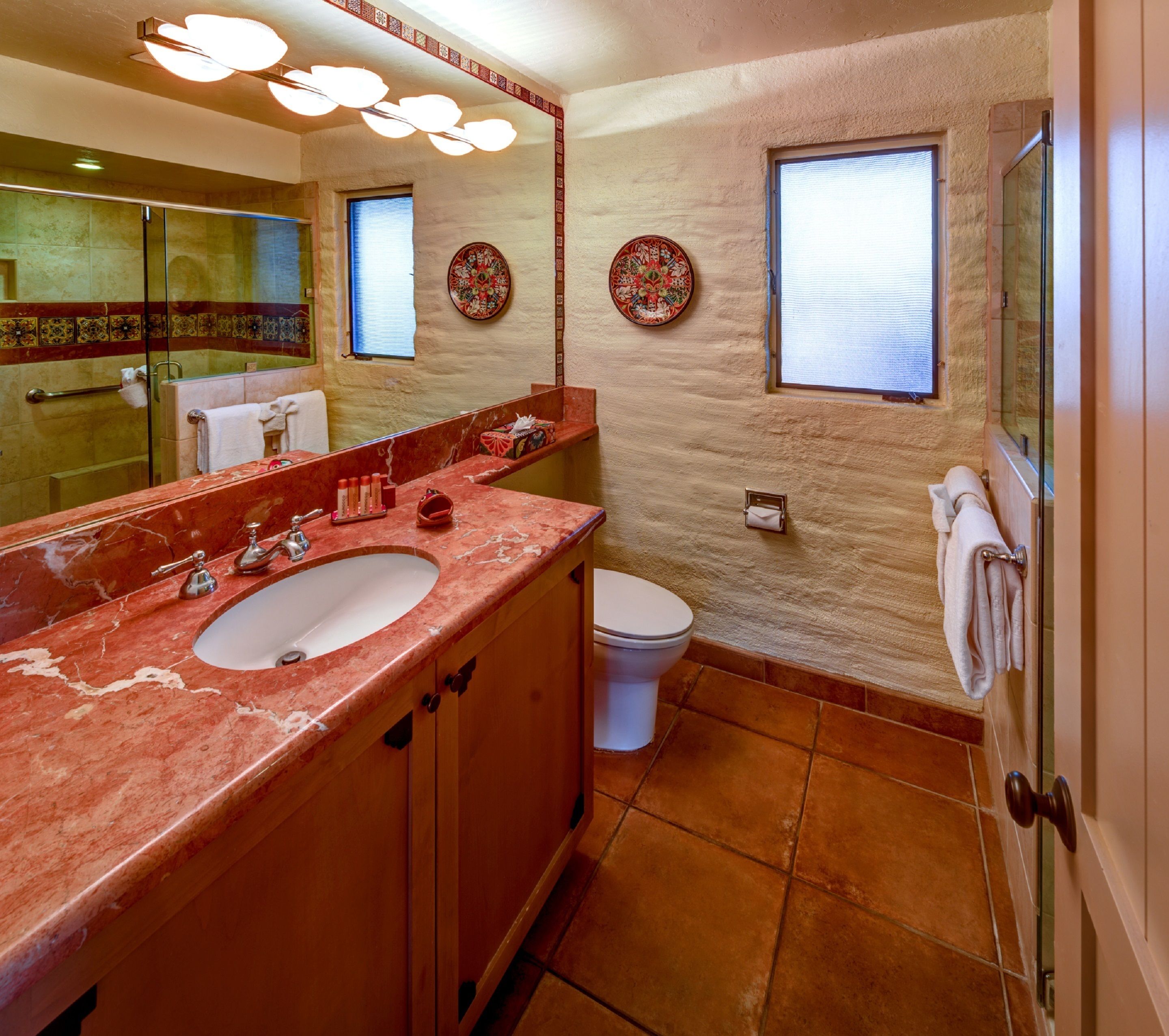 A bathroom with a marble sink, a toilet, and a shower. There are decorative plates on the walls and a towel rack.