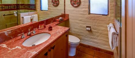 A bathroom with a marble sink, a toilet, and a shower. There are decorative plates on the walls and a towel rack.