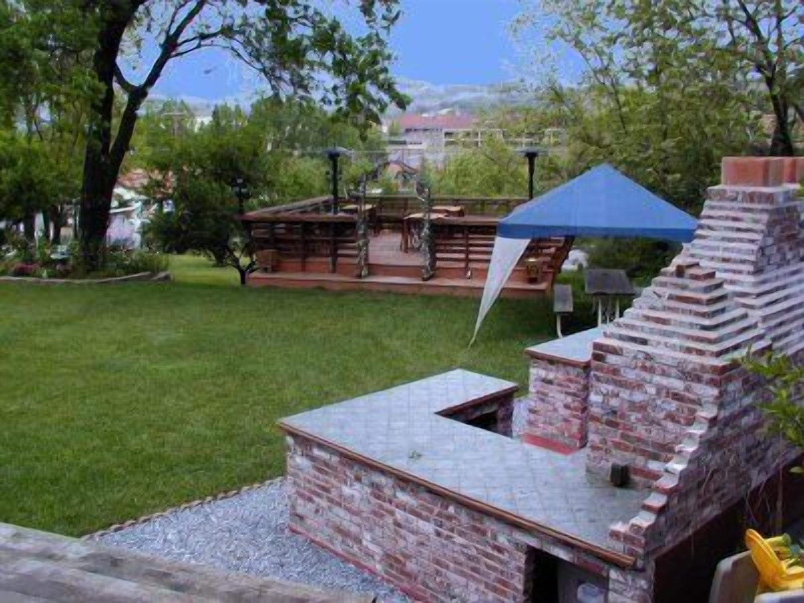A brick barbecue grill with a chimney, surrounded by a grassy lawn and trees.