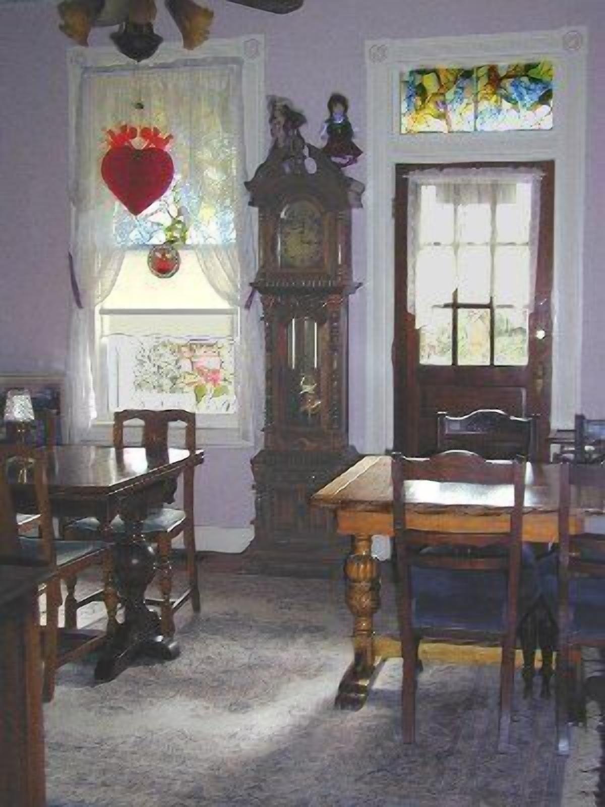 Une salle à manger avec une table et des chaises en bois, une grande horloge et une fenêtre ornée de vitraux.