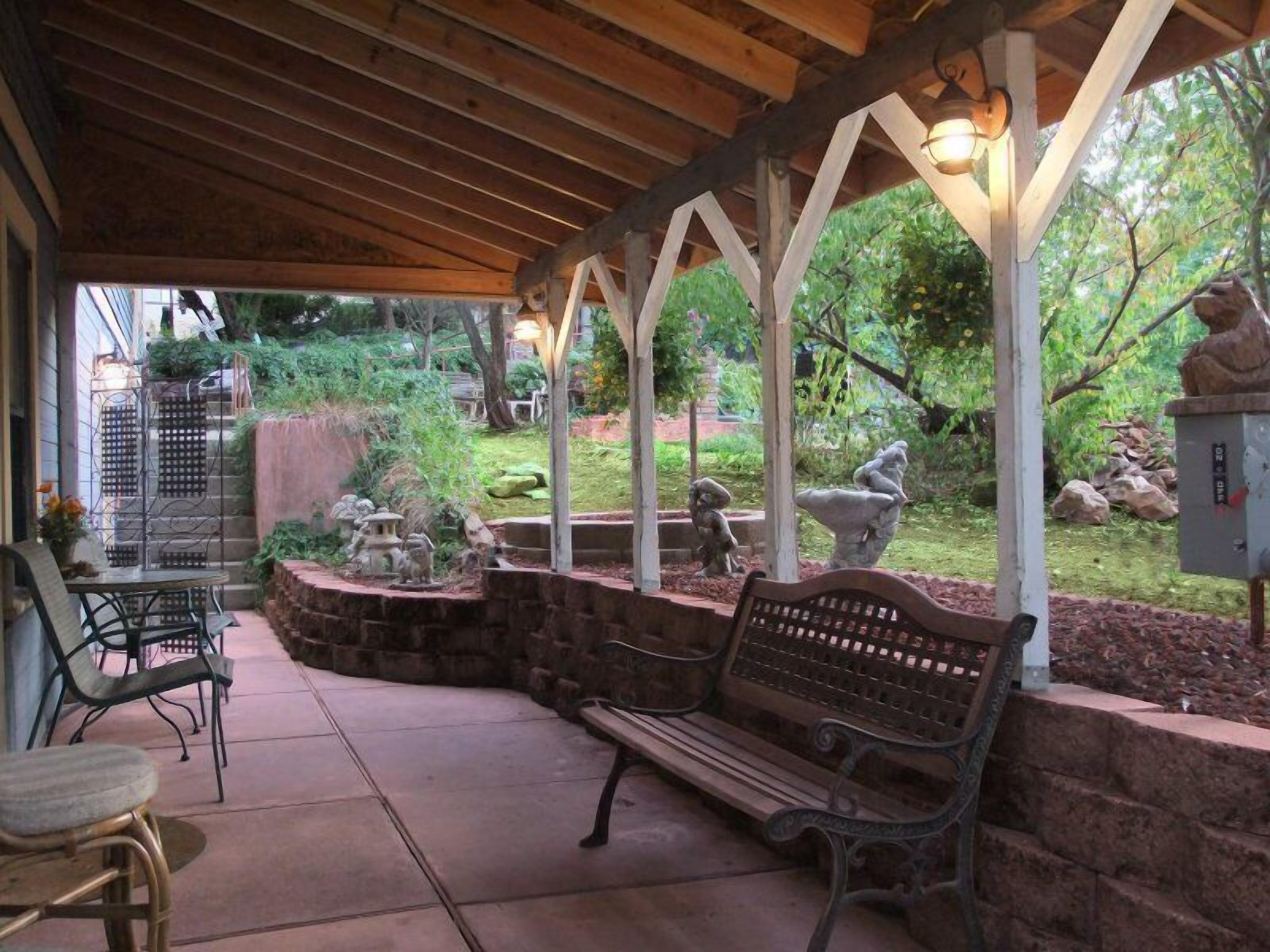 A covered patio area with a wooden bench, a table, and chairs.
