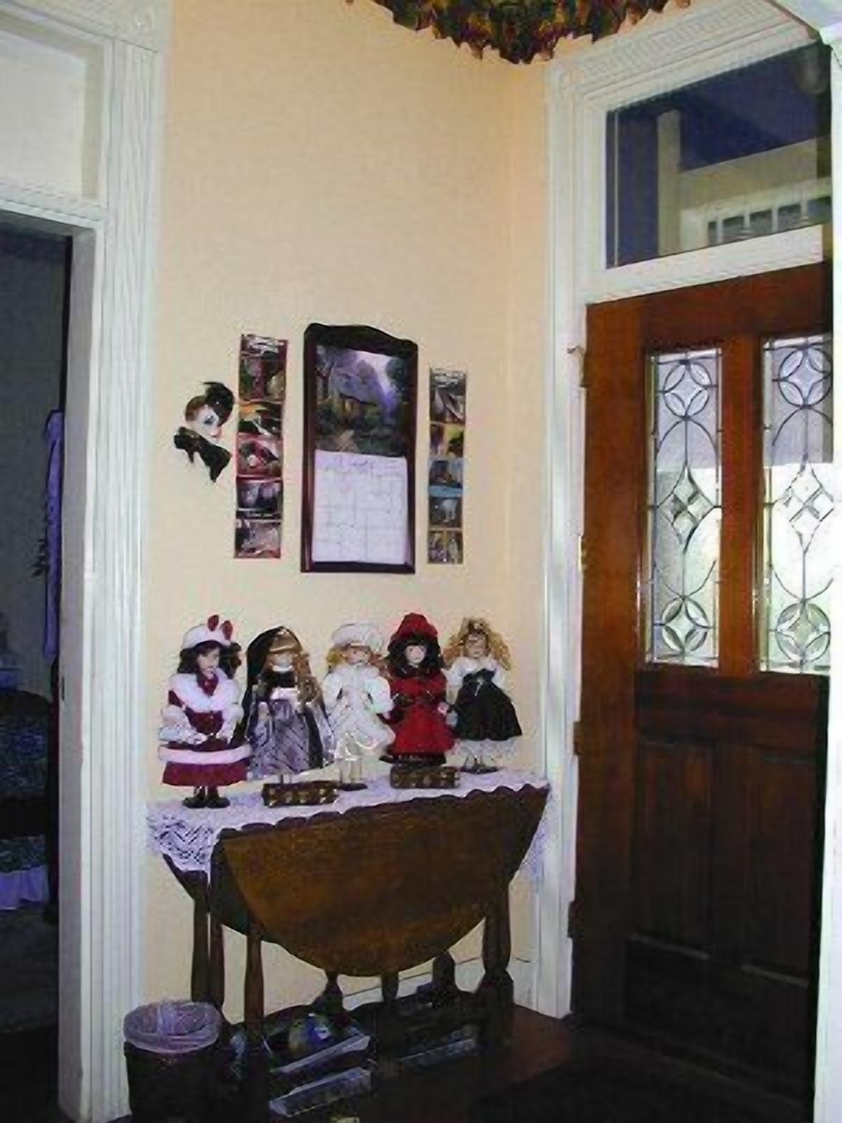 Una habitación con una mesa de madera mostrando figuritas, un cuadro en la pared y una ventana con rejas decorativas de hierro.