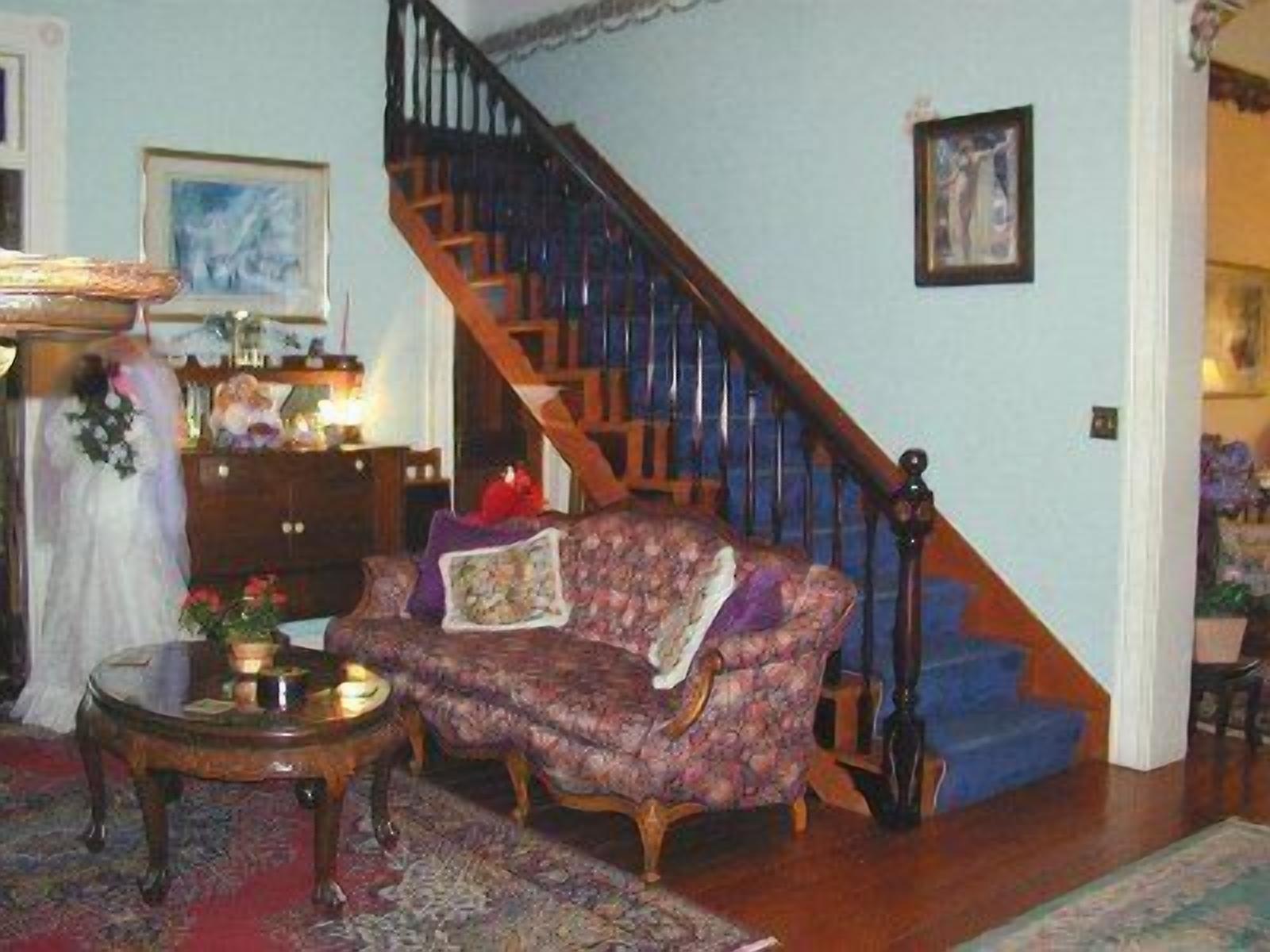 A living room with a patterned armchair, a small round table, and a staircase with wooden railings.