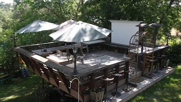 Un'area patio esterna con tavoli e sedie di legno, ombrelloni e una struttura bianca.