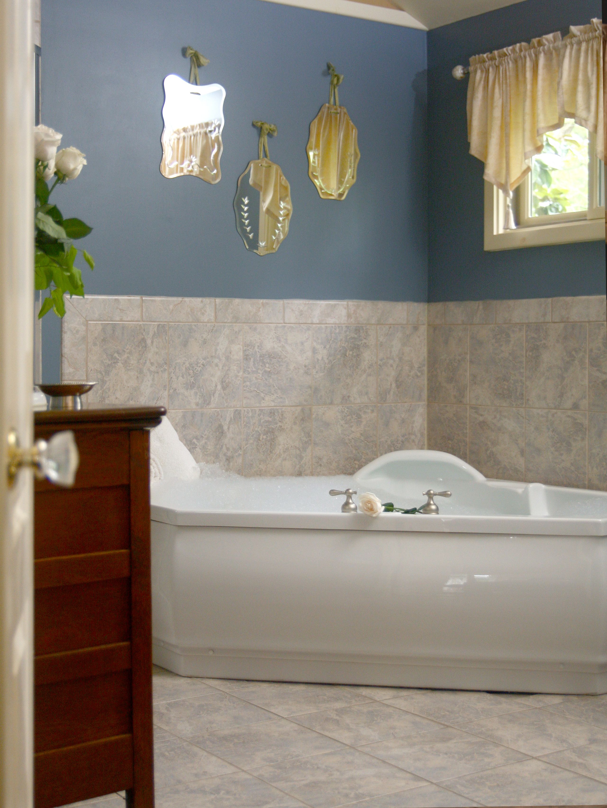 A bathroom with a bathtub, a wooden cabinet, and a window with curtains.