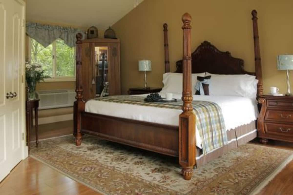 Een hemelbed met houten frame, een bijpassend nachtkastje, een dressoir en een raam met gordijnen.