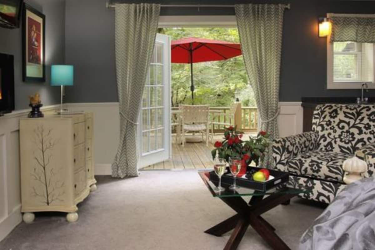 Een gezellige woonkamer met een open haard, een eettafel met een rode parasol, en een gestreept bankje.