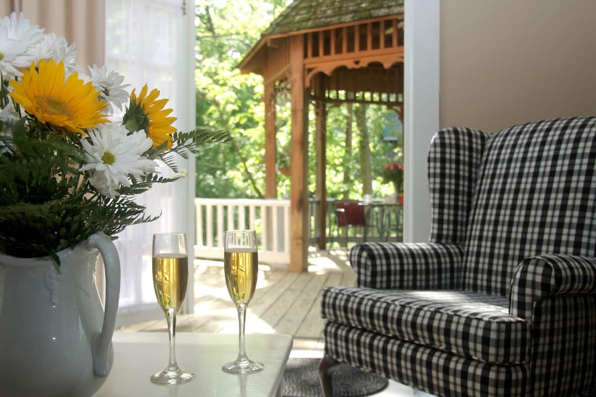Een kamer met een geruit sofa, een tafel met een bloemenvaas en twee glazen wijn, en uitzicht op een houten prieel op de achtergrond.