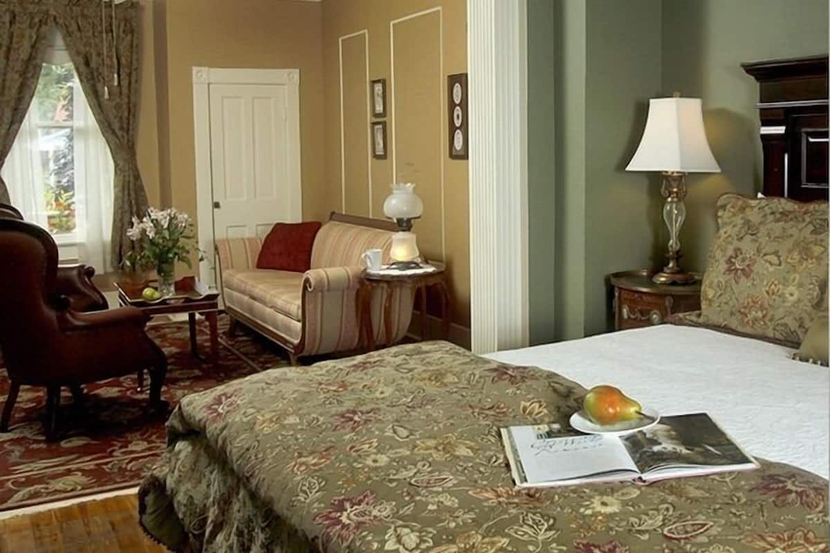 Een hotelkamer met een bed, een stoel, een tafel met een lamp en een raam met gordijnen.