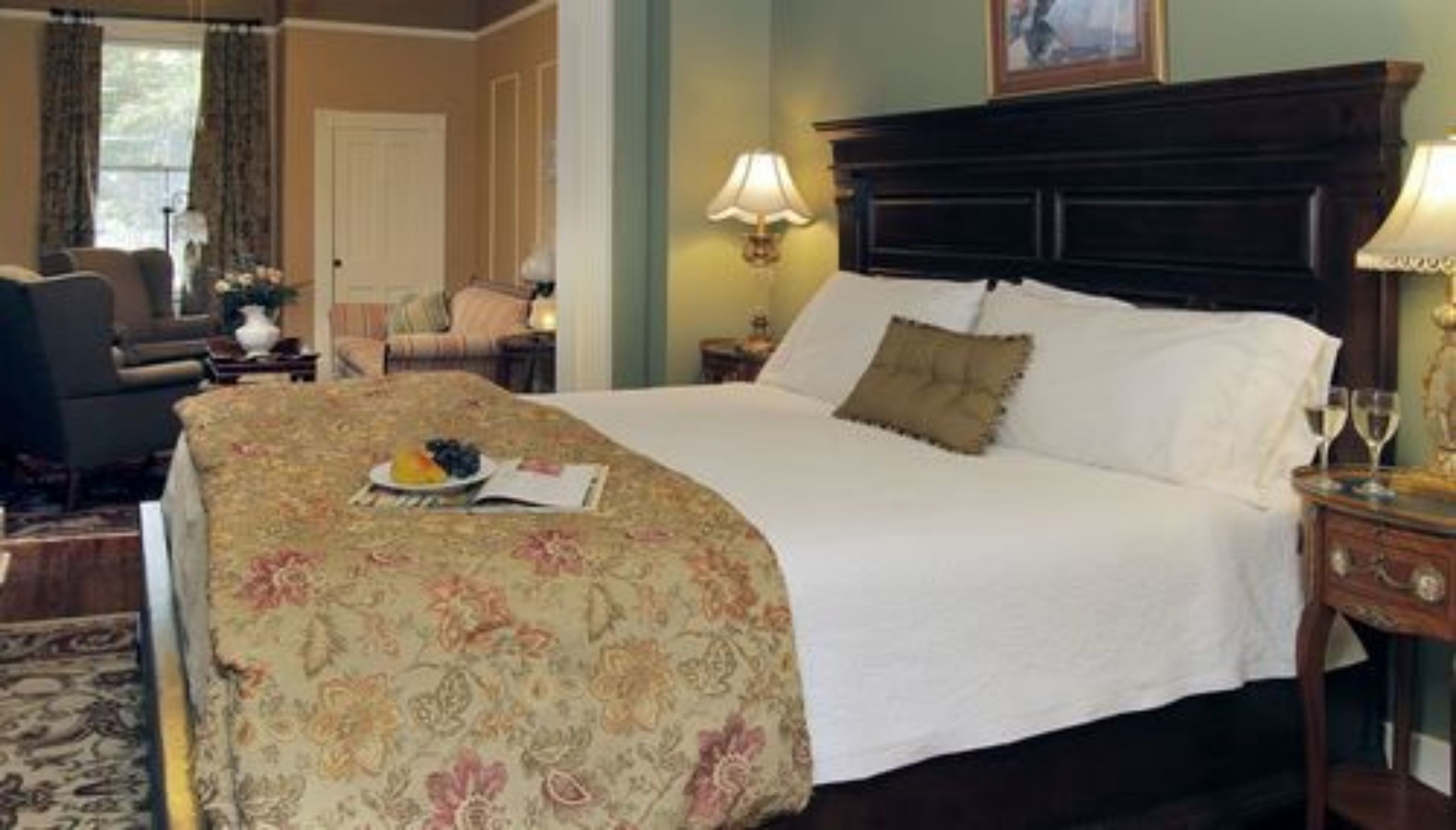 Un lit bien fait, recouvert d’une couvre-lit à motifs floraux, une table de chevet avec une lampe et une chaise dans une chambre d’hôtel.
