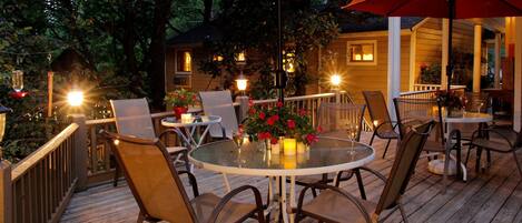 An outdoor patio with round tables and chairs, red umbrellas, and potted plants.