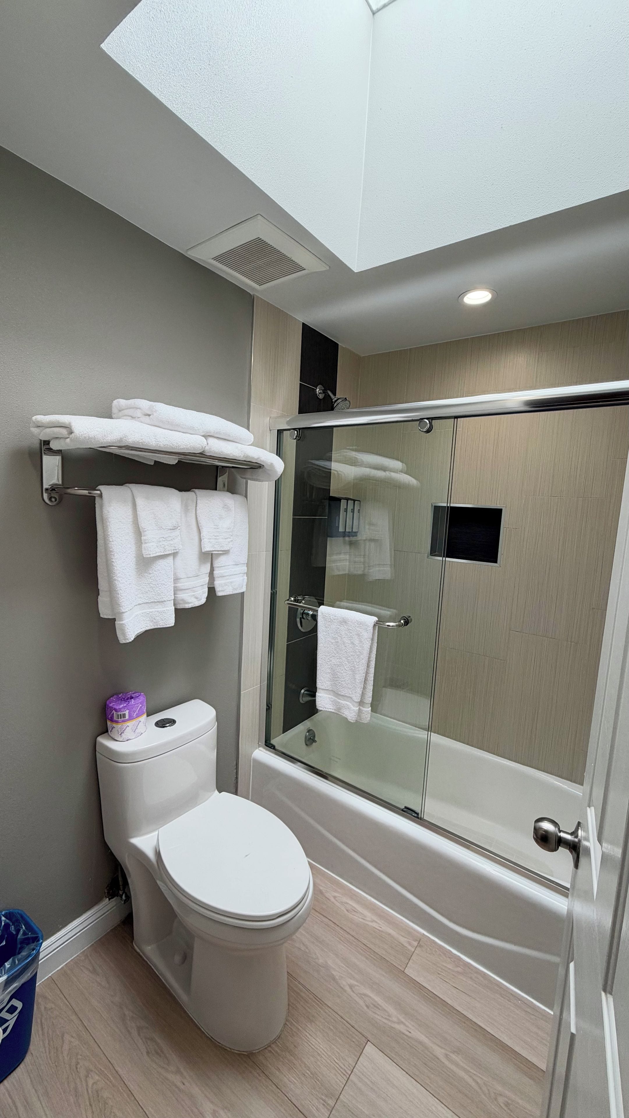 A modern bathroom with a toilet, a glass-enclosed shower, and a towel rack with folded towels.