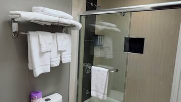 A modern bathroom with a toilet, a glass-enclosed shower, and a towel rack with folded towels.