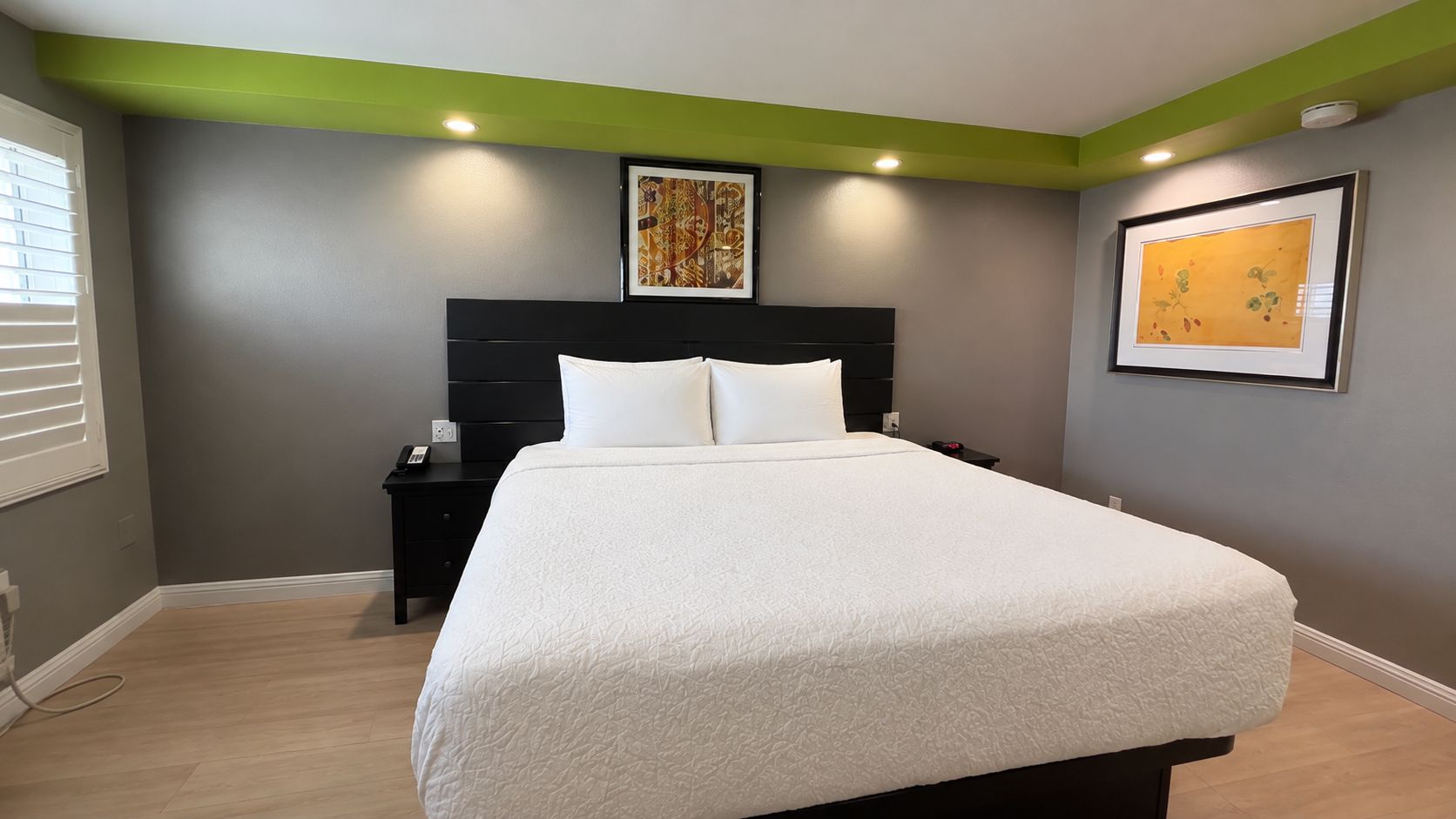 A bedroom with a bed, nightstand, and artwork on the walls.