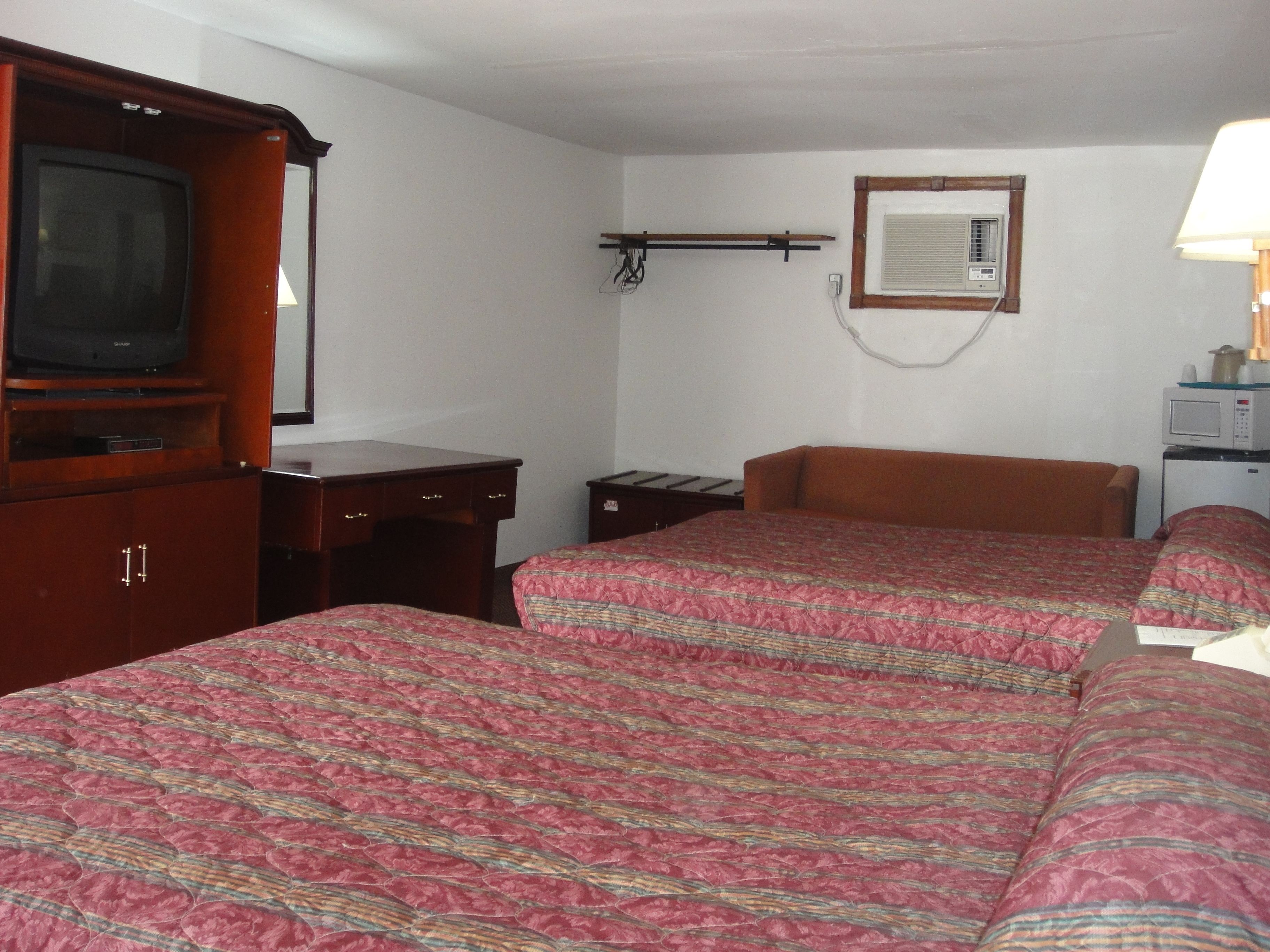 Habitación de hotel con dos camas, un armario de madera, un escritorio, televisor, espejo, calefacción y microondas.