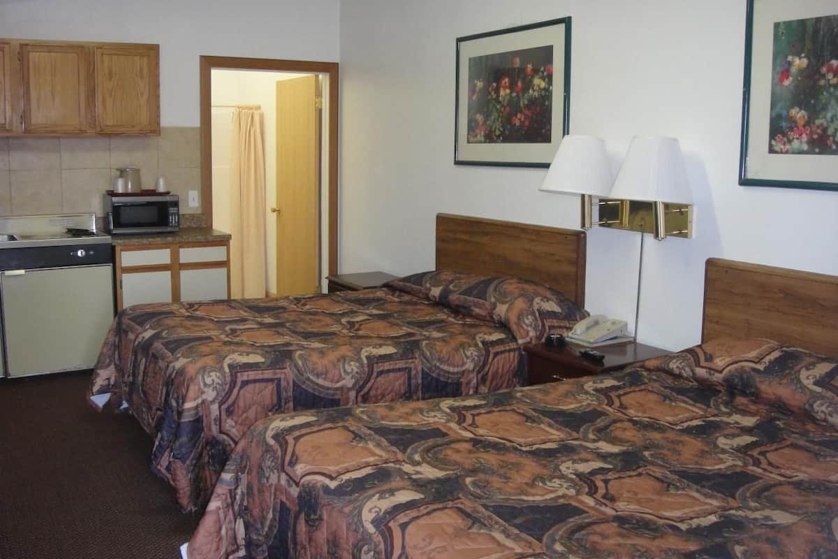 A hotel room with two beds, a kitchenette, and a bathroom.