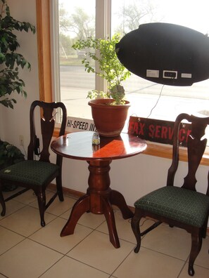 Una mesa redonda de madera con dos sillas, una planta en maceta y un cartel que dice 'Hi-Speed Internet' y 'Servicio de Fax'.