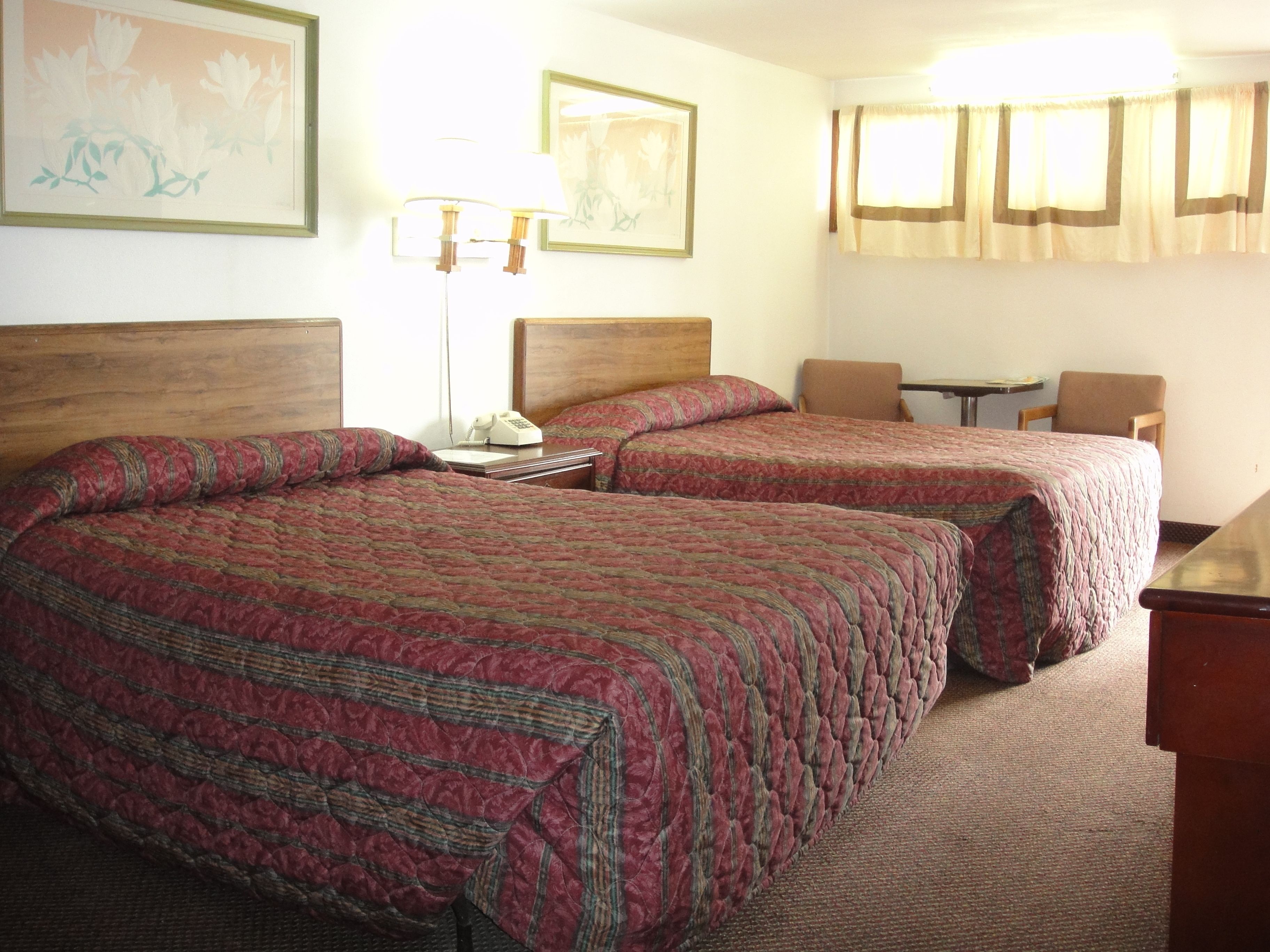 A hotel room with two beds, a desk, a chair, a lamp, and two framed pictures on the wall.