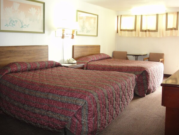 Habitación de hotel con dos camas, un escritorio, una silla, una lámpara y dos cuadros en la pared.