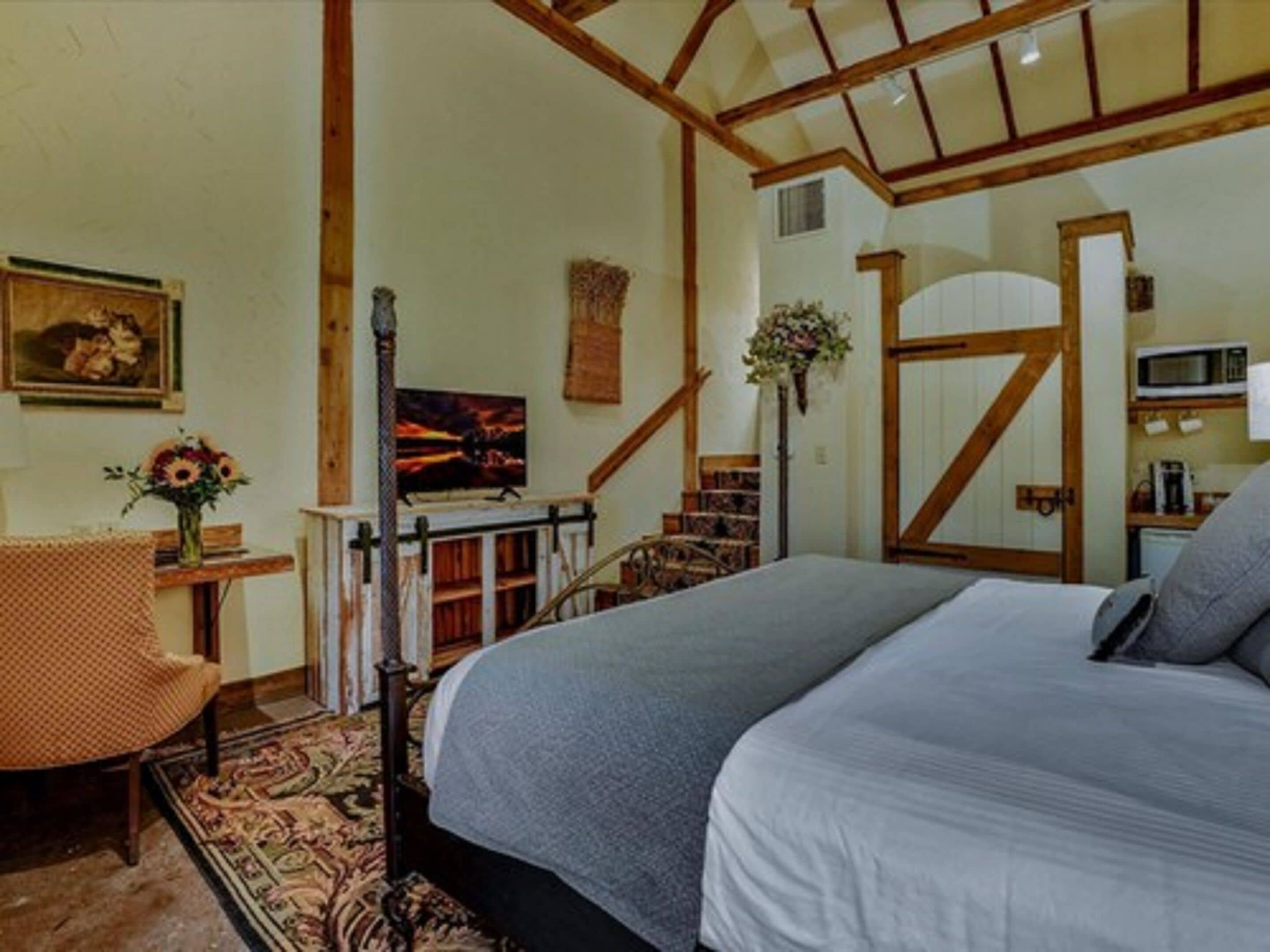 Un dormitorio con una cama grande, una escalera de madera, un pequeño escritorio con una silla y un cuadro en la pared.