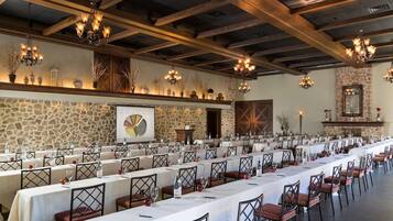 A long dining table set with white tablecloths and red chairs, surrounded by stone walls and wooden beams.