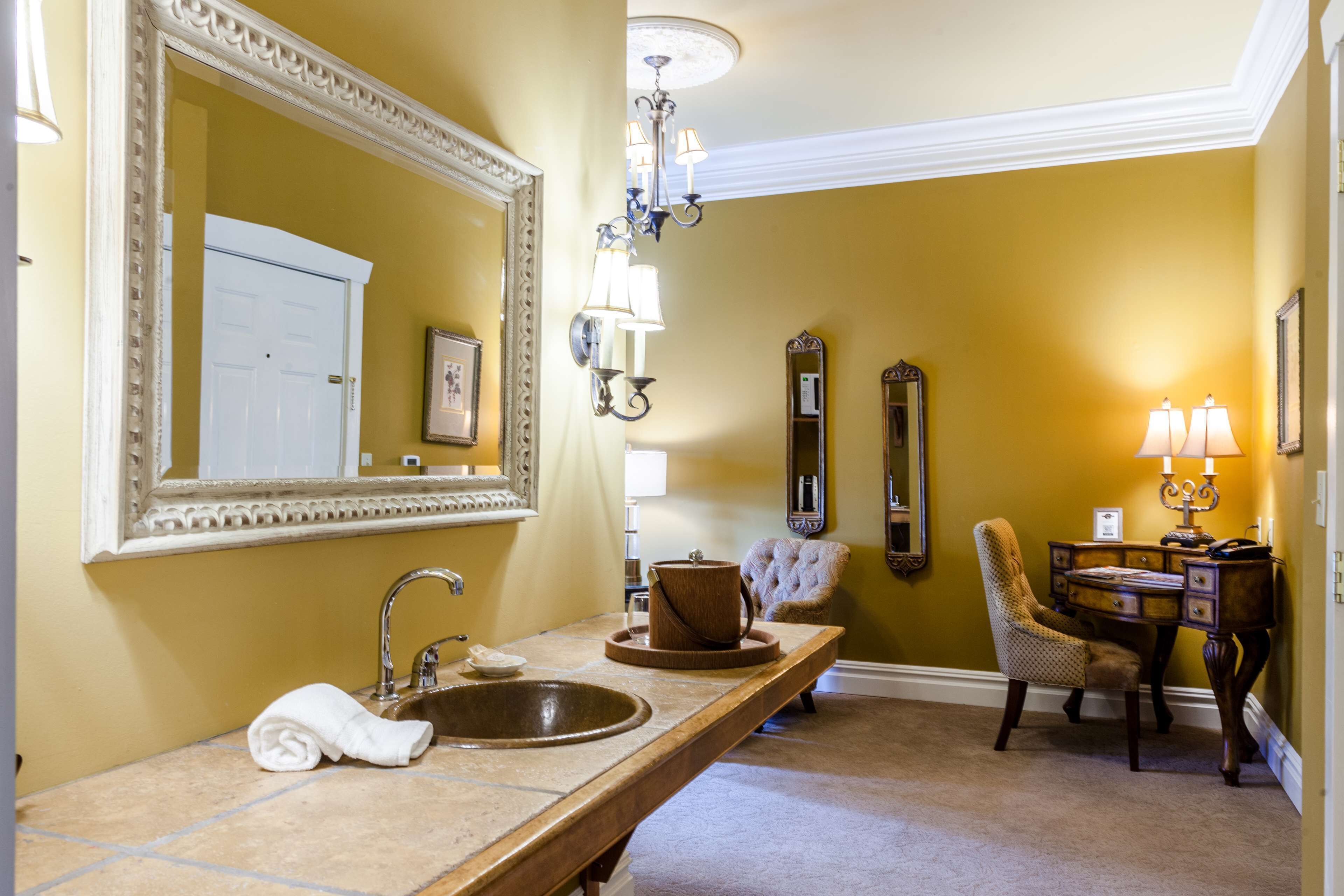 A bathroom with a large mirror, a sink, a chair, and a vanity table with lamps.