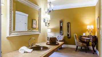 A bathroom with a large mirror, a sink, a chair, and a vanity table with lamps.