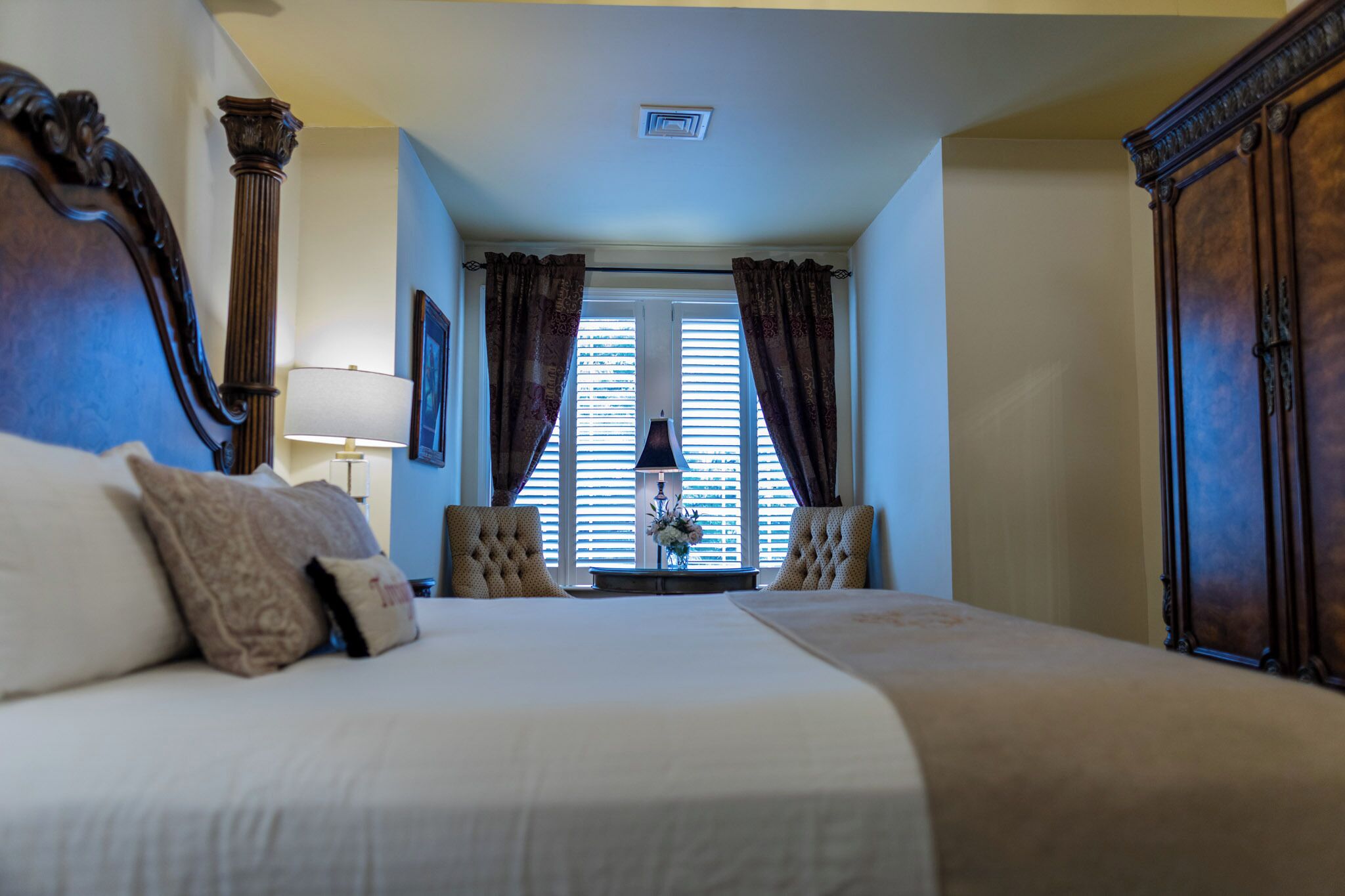 Una habitación de hotel con una cama grande, dos sillones, una mesita de noche y una ventana con persianas.