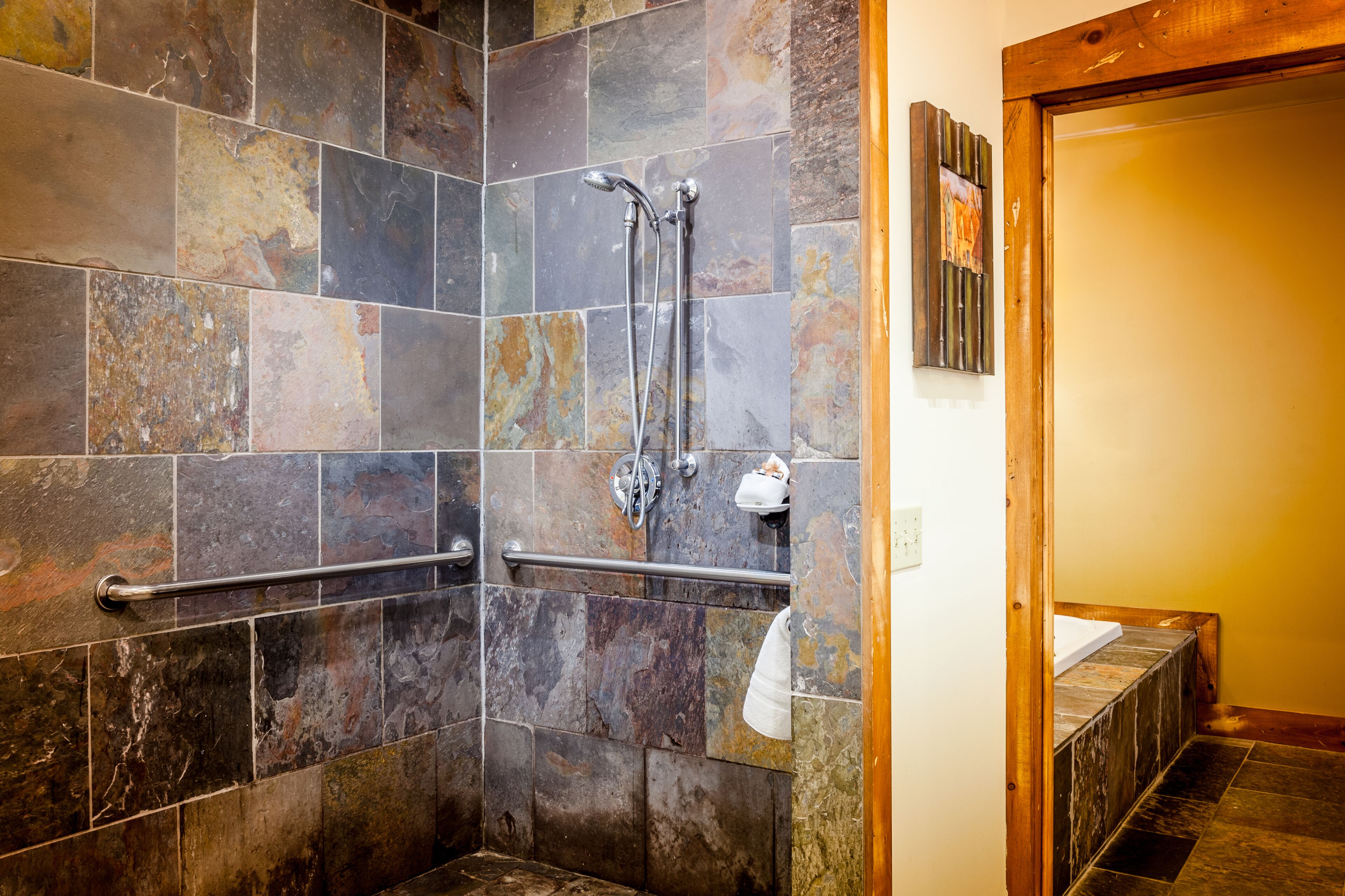 A shower area with a handrail, a towel rack, and a wooden frame around the shower door.