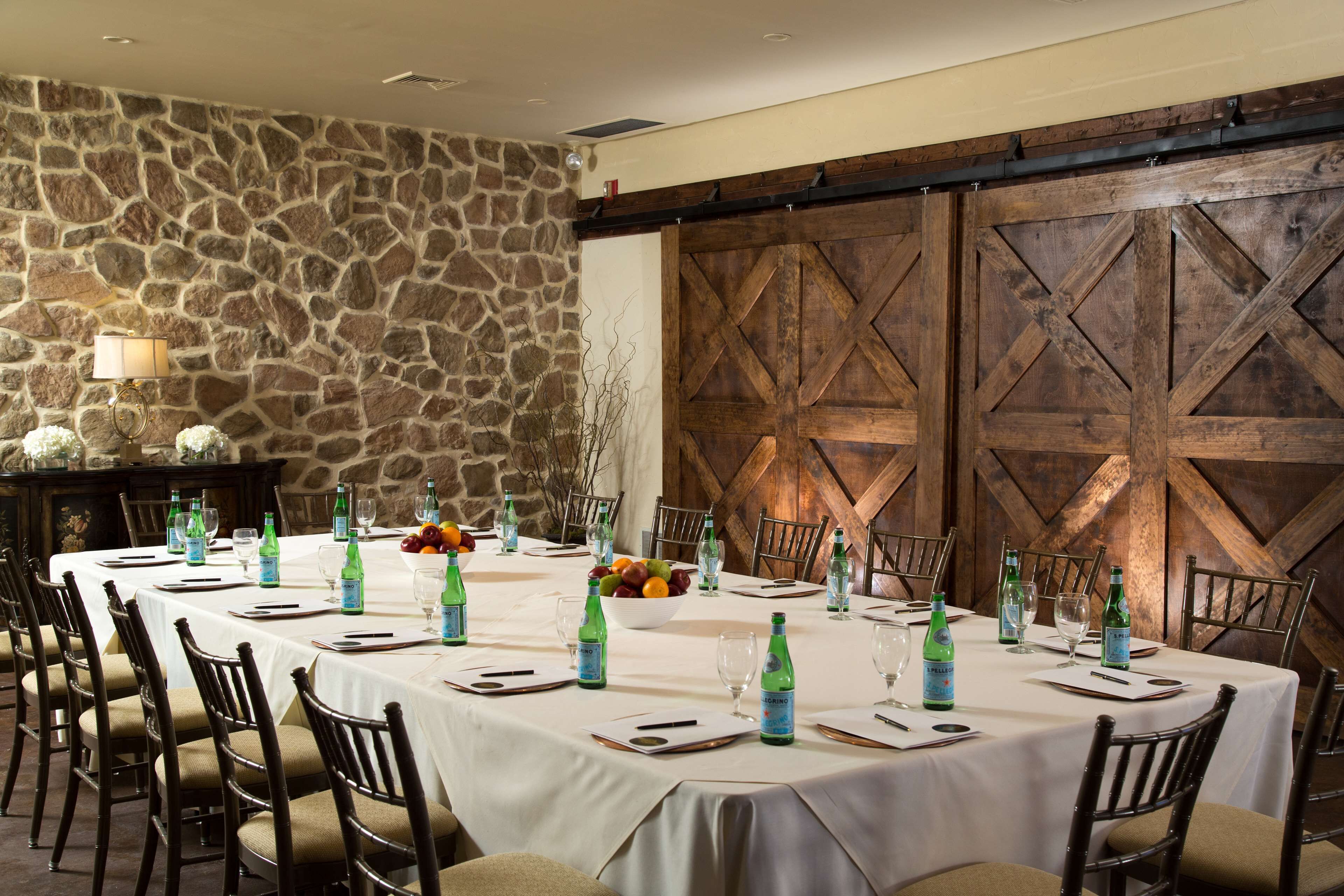 A dining area with a stone wall, wooden barn doors, and a long table set for a meal.