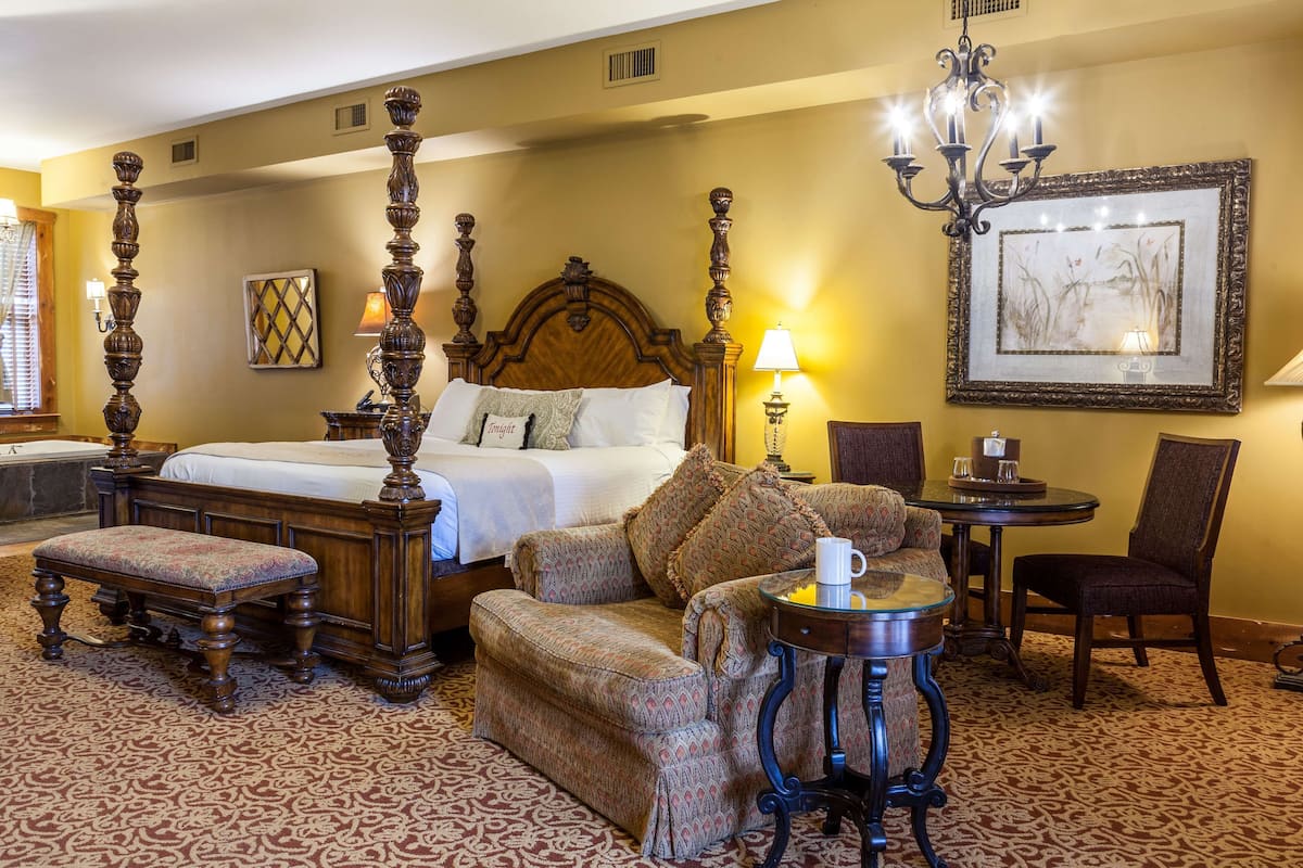 A hotel room with a large bed, a sofa, a small table, and a chair.