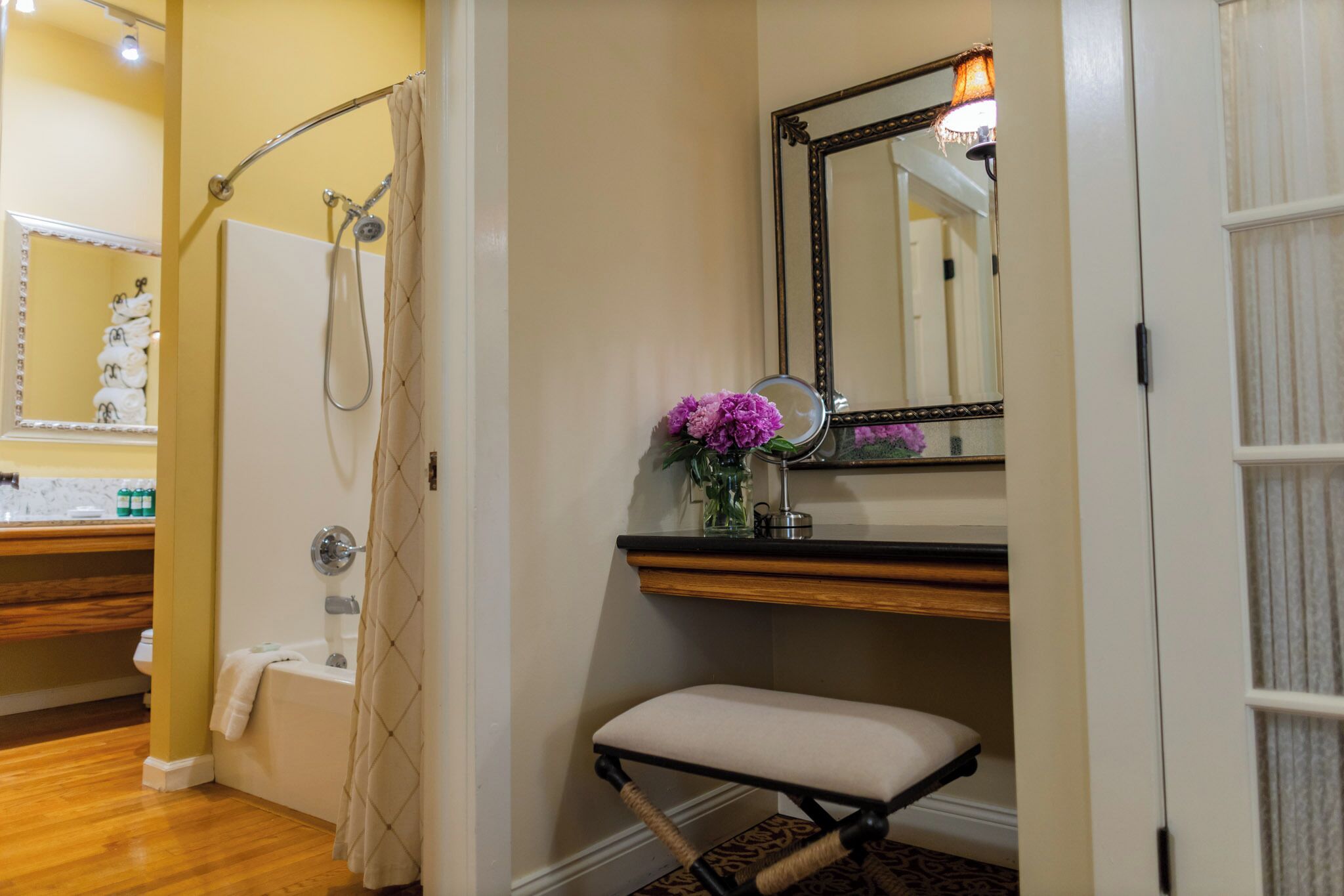 A bathroom with a shower, a vanity with a mirror, and a bench.