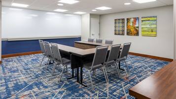 A conference room with a large table, chairs, a whiteboard, and three paintings on the wall.
