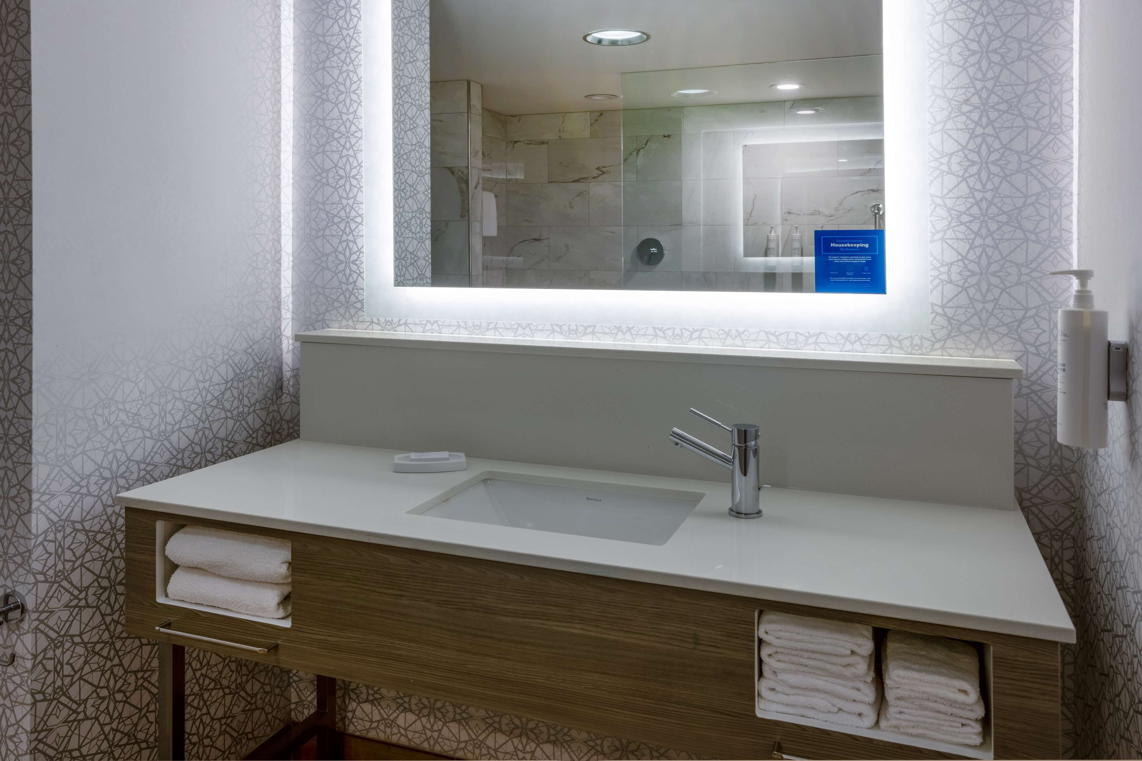 A modern bathroom with a large mirror, a white sink, and a towel rack.