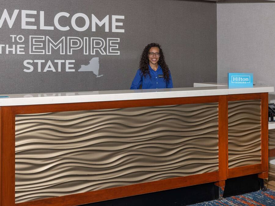 Ein Empfangsschalter mit einem Schild mit der Aufschrift "WELCOME TO THE EMPIRE STATE", einem Hilton Honors-Schild und einer Holzvertäfelung.