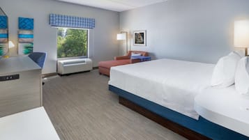 A hotel room with a large bed, a desk, a chair, and a window with a view of trees.